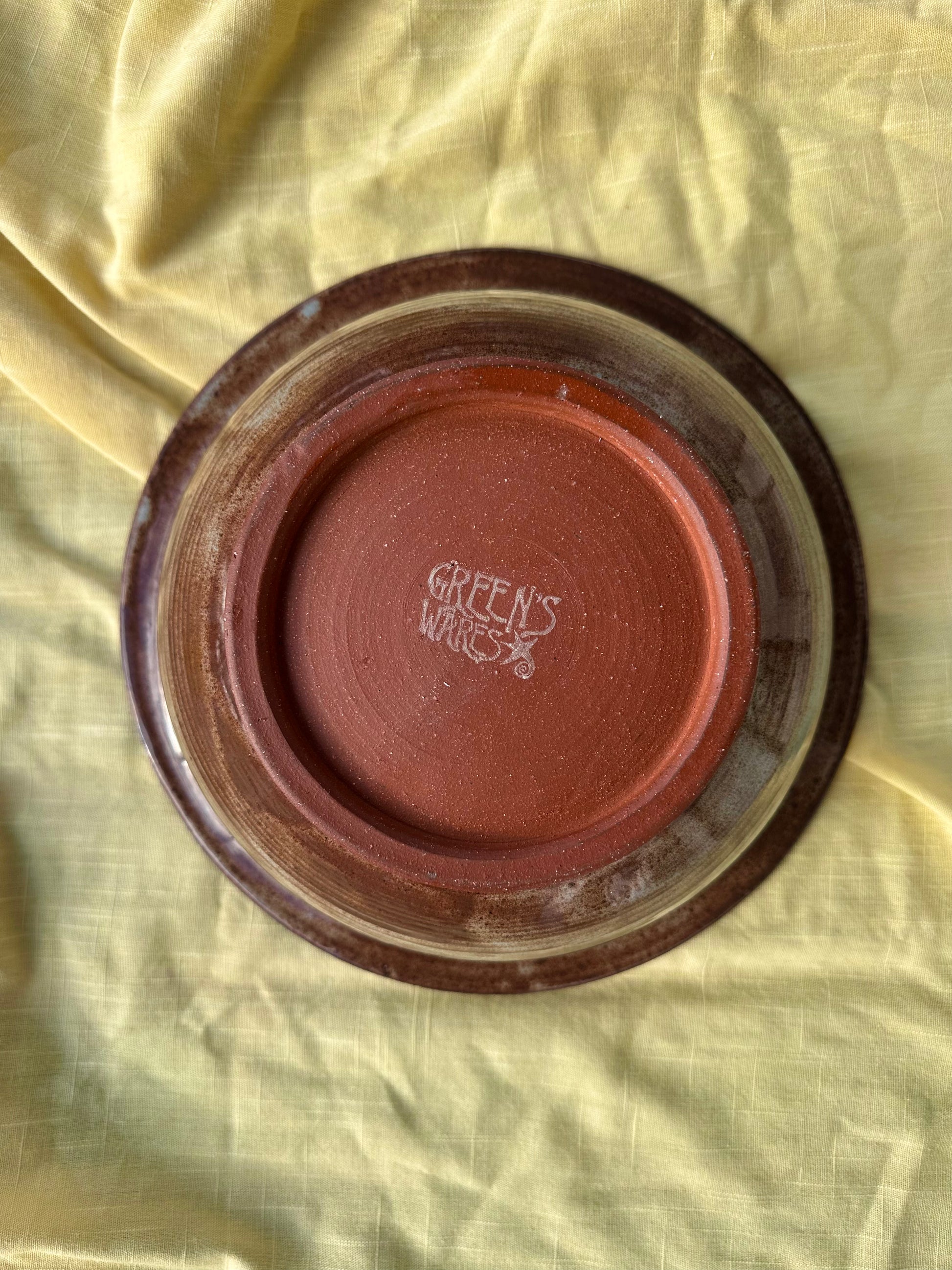 Bottom of a ceramic bowl with red clay and "Green's Wares" branded stamp in the center.