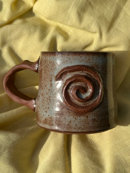 Ceramic mug with light blue and brown glaze, and a raw clay spiral and handle.