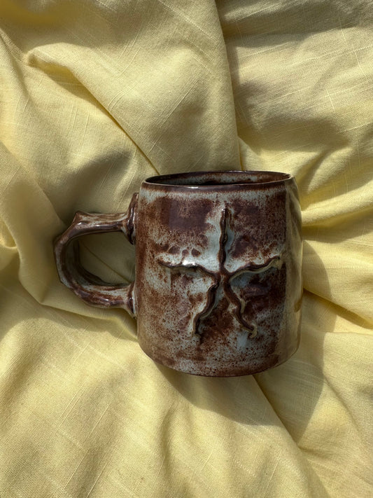 Ceramic mug with a textured star on the surface, the glaze is a dark brown with highlights of light blue.